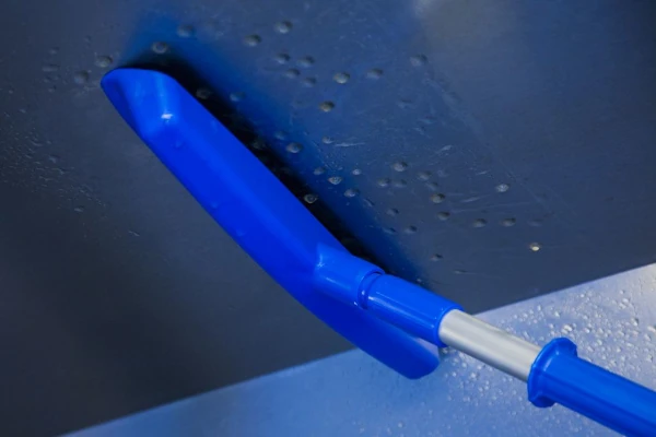 Condensation squeegee removing droplets from an overhead panel in a food facility to prevent contamination.