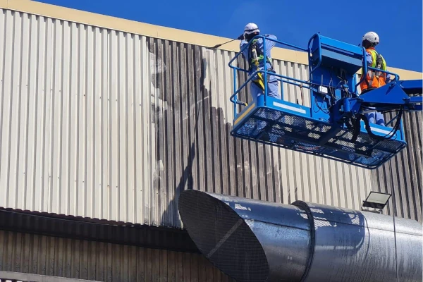 Ecowize technicians on a boom lift performing high-level specialised cleaning of exterior cladding at a food facility, wearing full fall-protection.