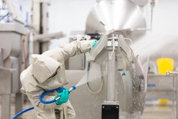An Ecowize Food processing sanitation worker cleaning equipment with high-pressure hose and PPE in a controlled hygiene environmen