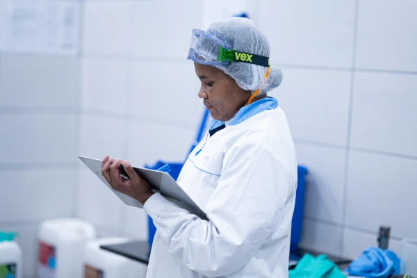 Food processing worker in protective clothing reviewing a sanitation checklist on a tablet inside a hygienic production facility.