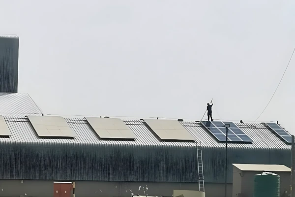Industrial building with solar panels installed on a corrugated metal roof, with a worker performing maintenance near the rooftop solar array.