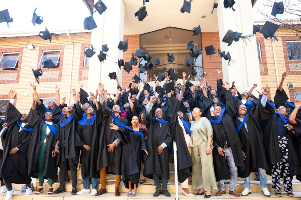 Ecowize graduates celebrating their achievement at a graduation ceremony, throwing their mortarboard caps into the air outside a university building.